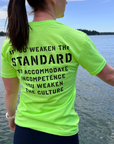 Person wearing a bright green t-shirt with text by a body of water