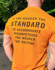 Man wearing an orange t-shirt with a motivational message on the back, standing outdoors.
