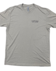 A stone gray crewneck t-shirt with a small black 'Comfortable with chaos' logo printed on the left chest, displayed flat against a white background.