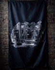 A black flag featuring a white graphic illustration of skeleton figures standing beside a vintage police vehicle, hanging against a dark brick wall.