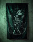 A dark gothic wall flag featuring a white skeleton walking on a road under a full moon, hung on a textured green wall.