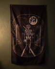 A dark gothic wall flag featuring a skeleton walking down a road under a full moon, hung on a dark textured wall.