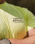 Person wearing a bright yellow t-shirt with 'Lurkin Apparel' branding, outdoors.