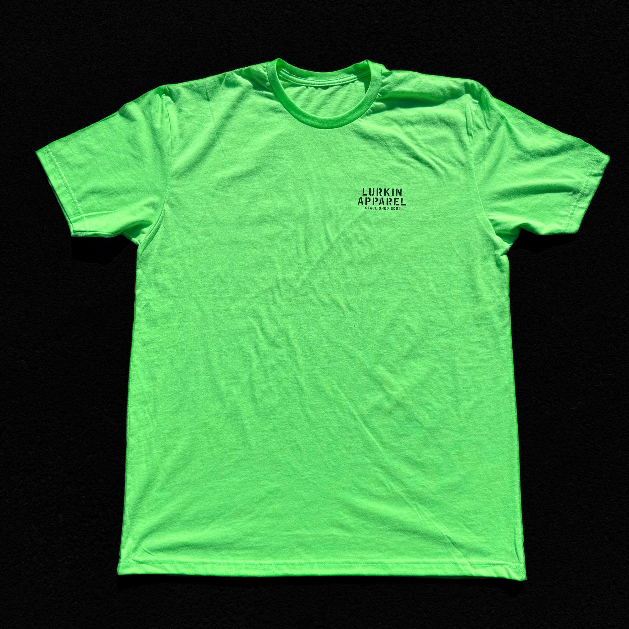 Green t-shirt with a small logo on a black background