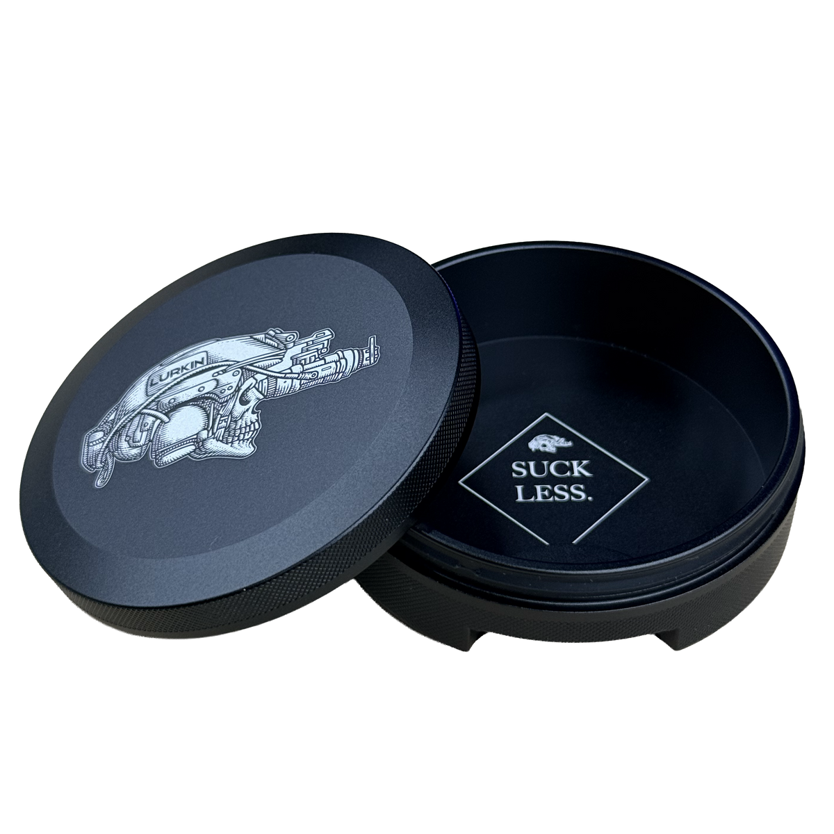 A black round metal tin with its lid leaning against it on a white background. The lid features a graphic of a logo while the inside of the tin is also black with a logo that reads 'SUCK LESS.