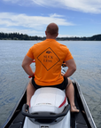 Person sitting on a jet ski wearing an orange shirt with text, looking out over water.