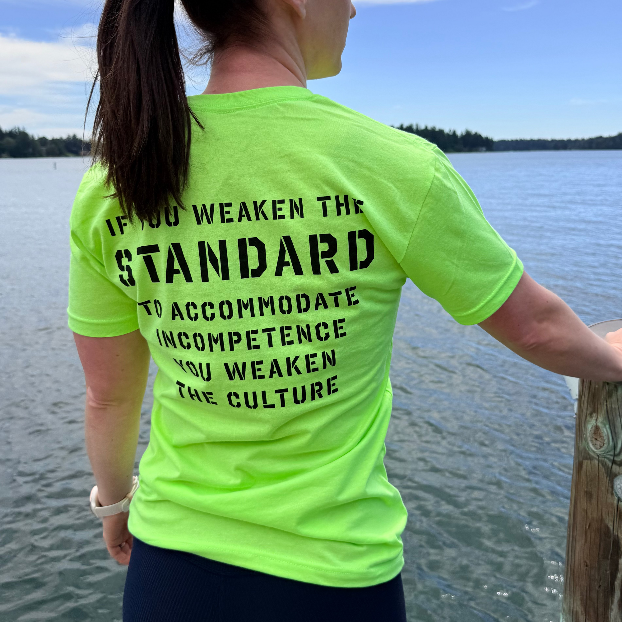 Person wearing a bright green t-shirt with text by a body of water