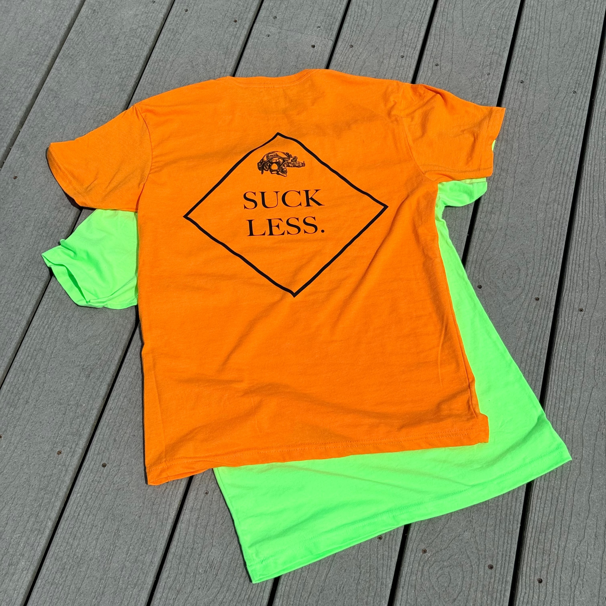 Orange t-shirt with 'Suck Less' text on a gray wooden surface