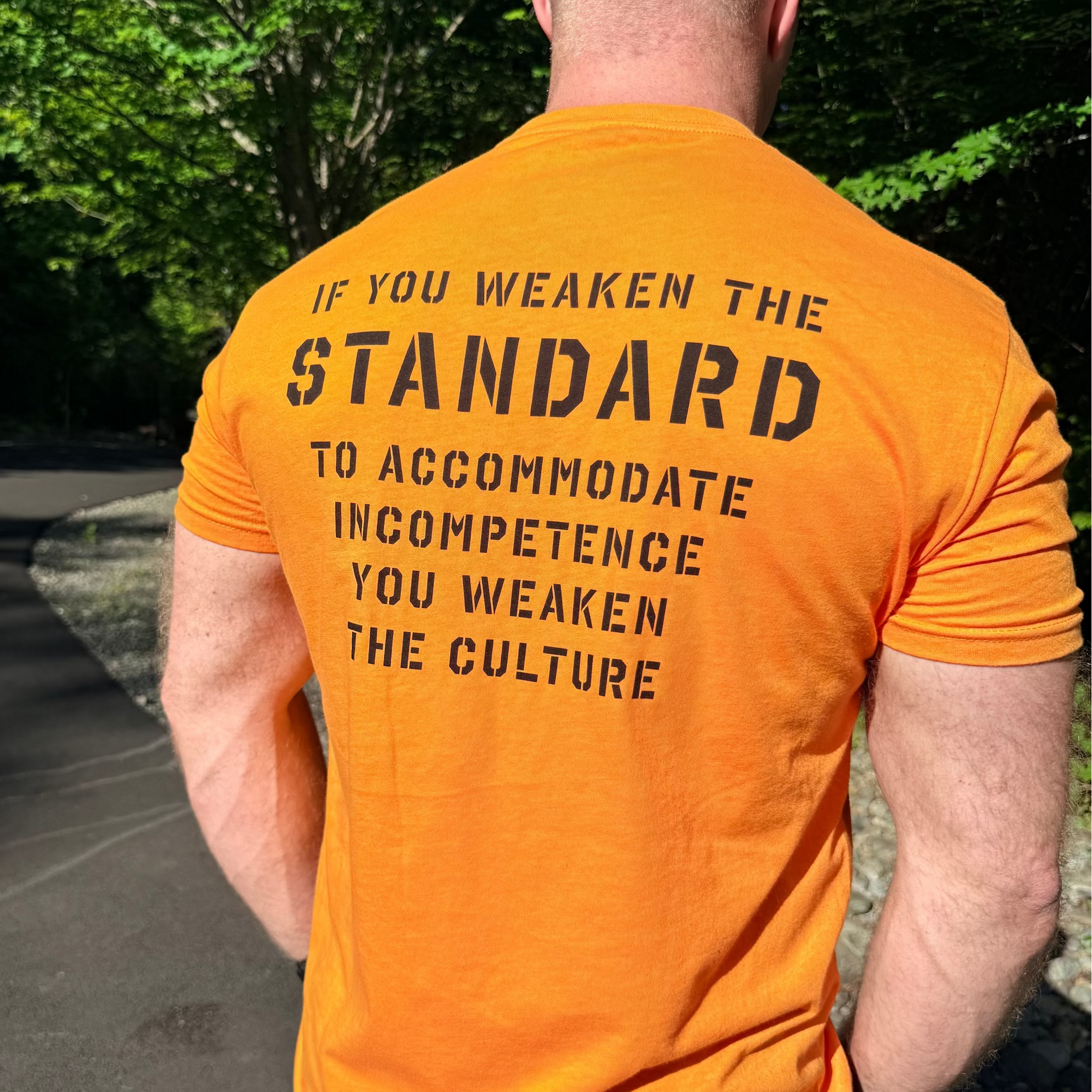 Man wearing an orange t-shirt with a motivational message on the back, standing outdoors.