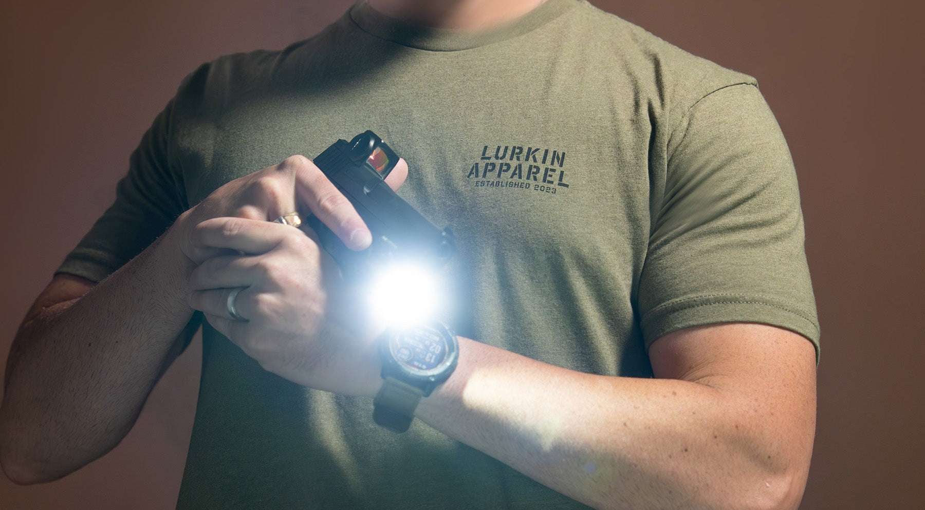 Man holding a flashlight wearing a green t-shirt with text on it against a brown background