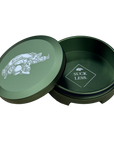 A olive drab round metal tin with its lid leaning against it on a white background. The lid features a graphic of a logo while the inside of the tin is also olive drab with a logo that reads 'SUCK LESS.