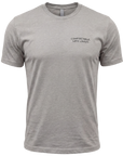 A stone gray short-sleeve crewneck t-shirt with the text 'COMFORTABLE WITH CHAOS' printed in black script on the left chest, displayed on a clean white background.