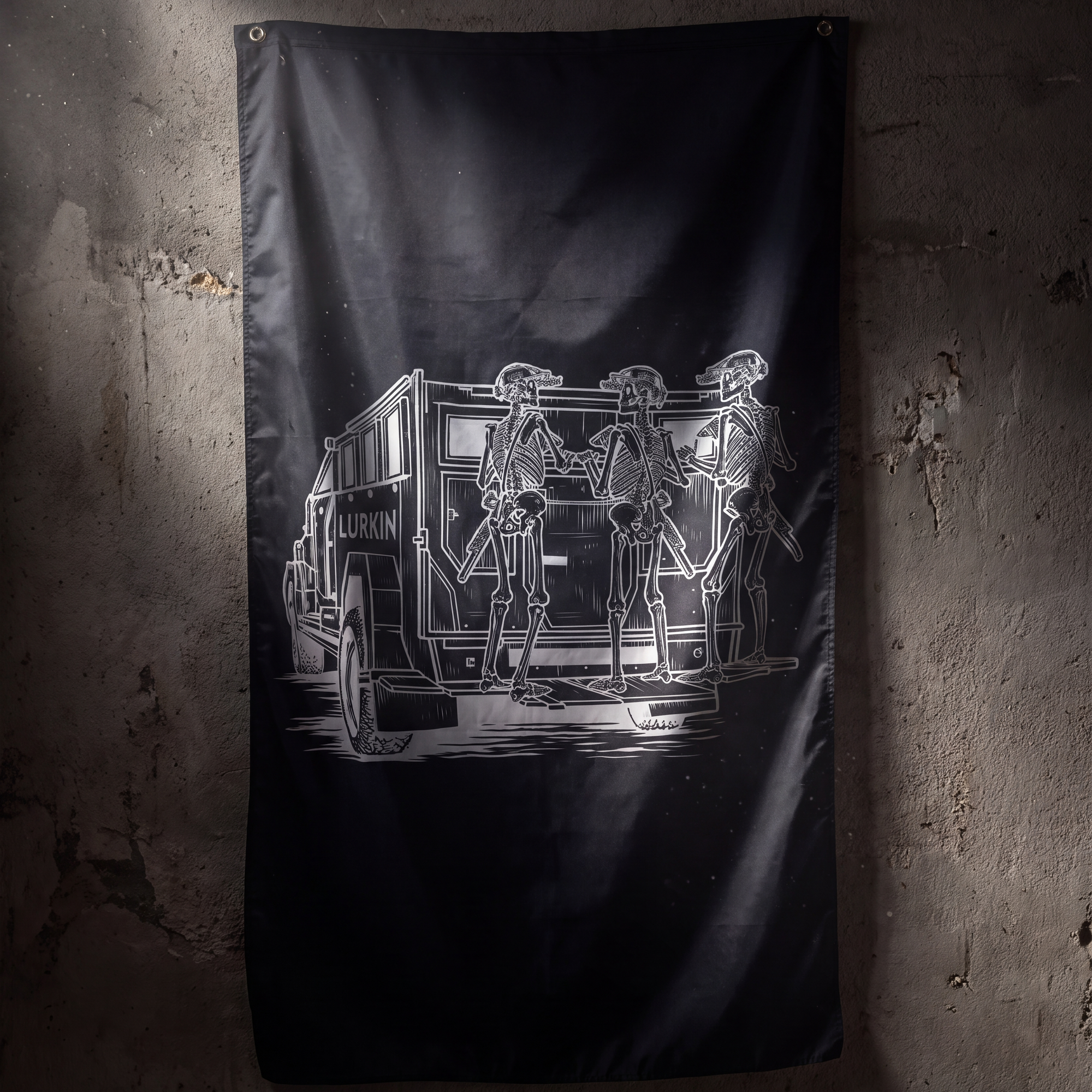 A black flag hanging on a textured concrete wall, featuring a white graphic illustration of skeleton figures standing beside a truck with the word 'LURKIN' on the side.