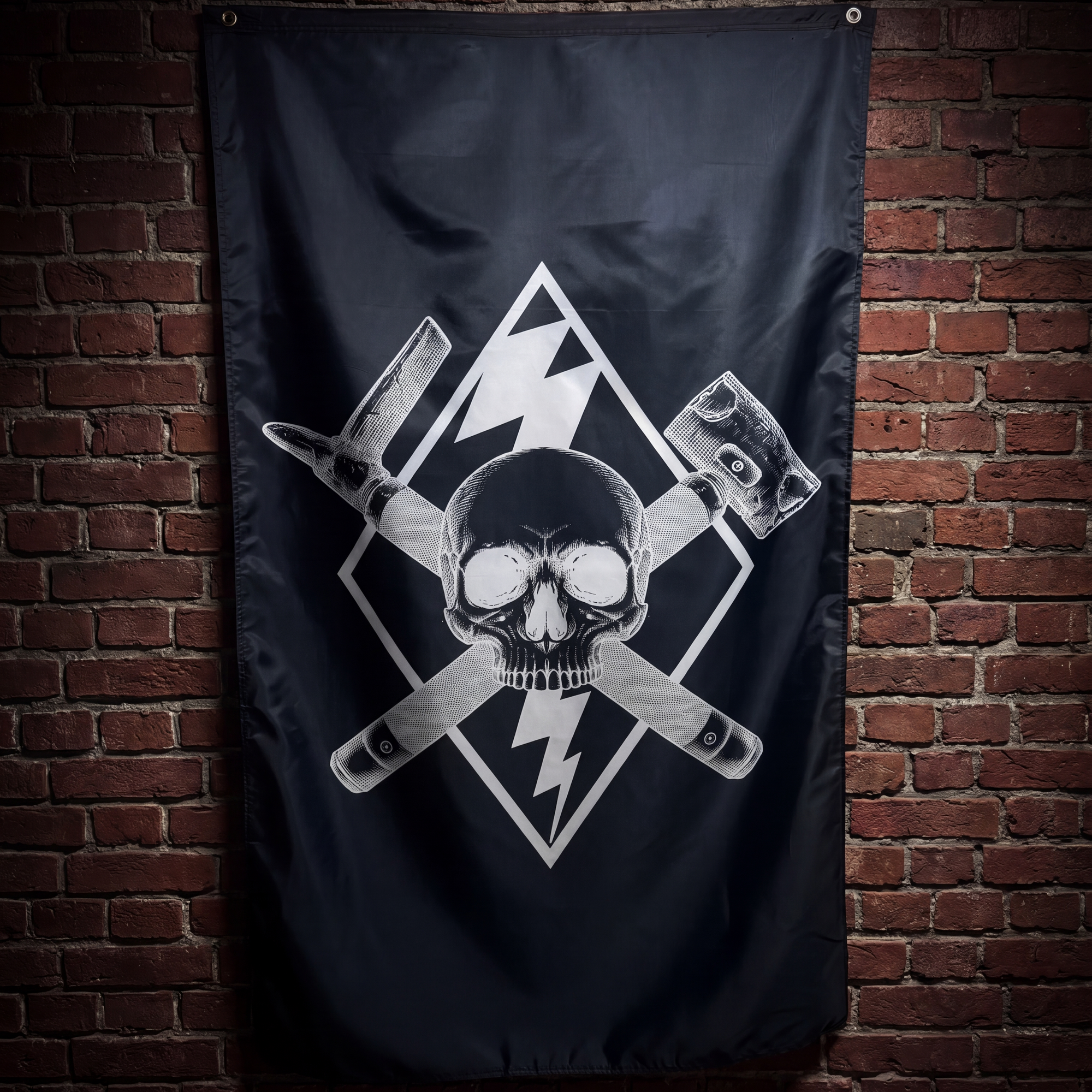 A black flag featuring a white skull and crossed tools graphic, hanging against a red-brown brick wall.