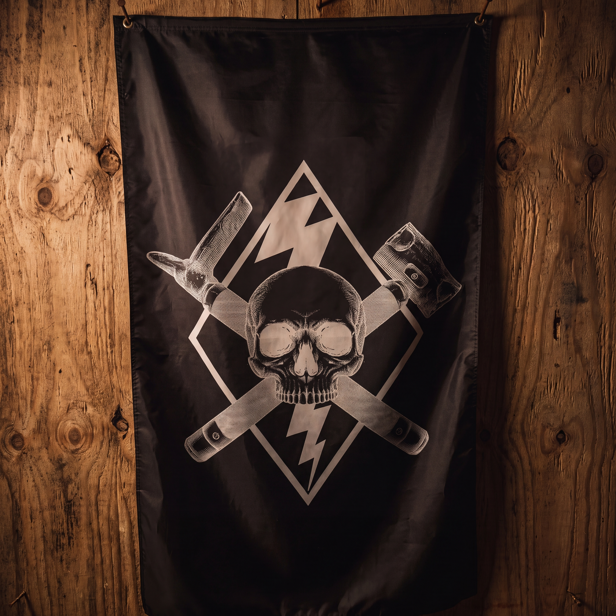 A black flag featuring a white skull and crossed tools graphic, hanging against a rustic wooden plank wall.