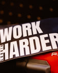 Sticker with 'Work Harder' text on a blurred background