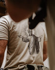 A close-up lifestyle shot of a person wearing a beige t-shirt with a black graphic of Jesus Christ on the back wearing night vision. 