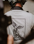 A man viewed from behind wearing a tactical helmet and a light gray t-shirt featuring a large black graphic of an angel on the back. 
