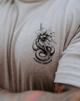 Close-up of a person wearing a light tan t-shirt with a black graphic of a coiled snake and the text 'Lurkin Apparel' printed on the chest.