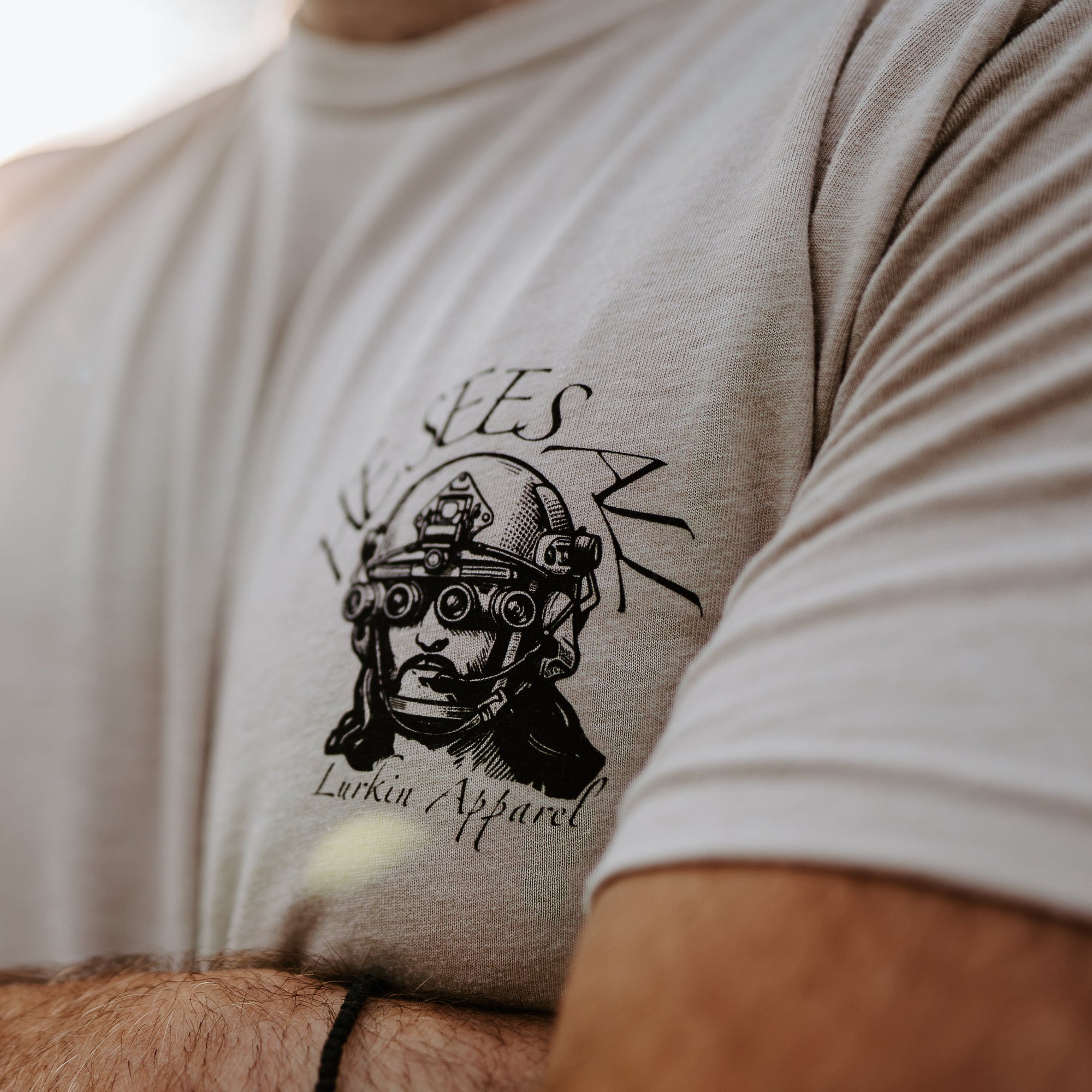 Close-up of a person wearing a light beige t-shirt with a black graphic print of a helmeted figure.