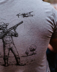 A man wearing a heather gray t-shirt with a black graphic of a skeleton cowboy holding a shotgun under a drone.
