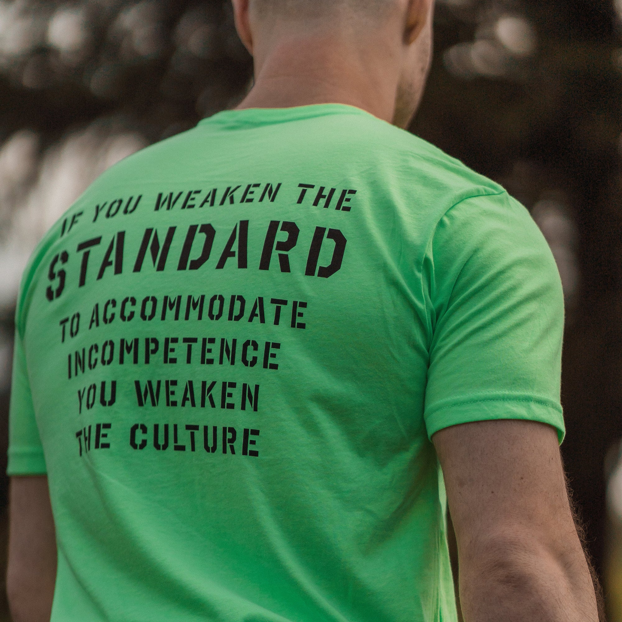 Person wearing a neon green t-shirt with a motivational message on the back, standing outdoors.
