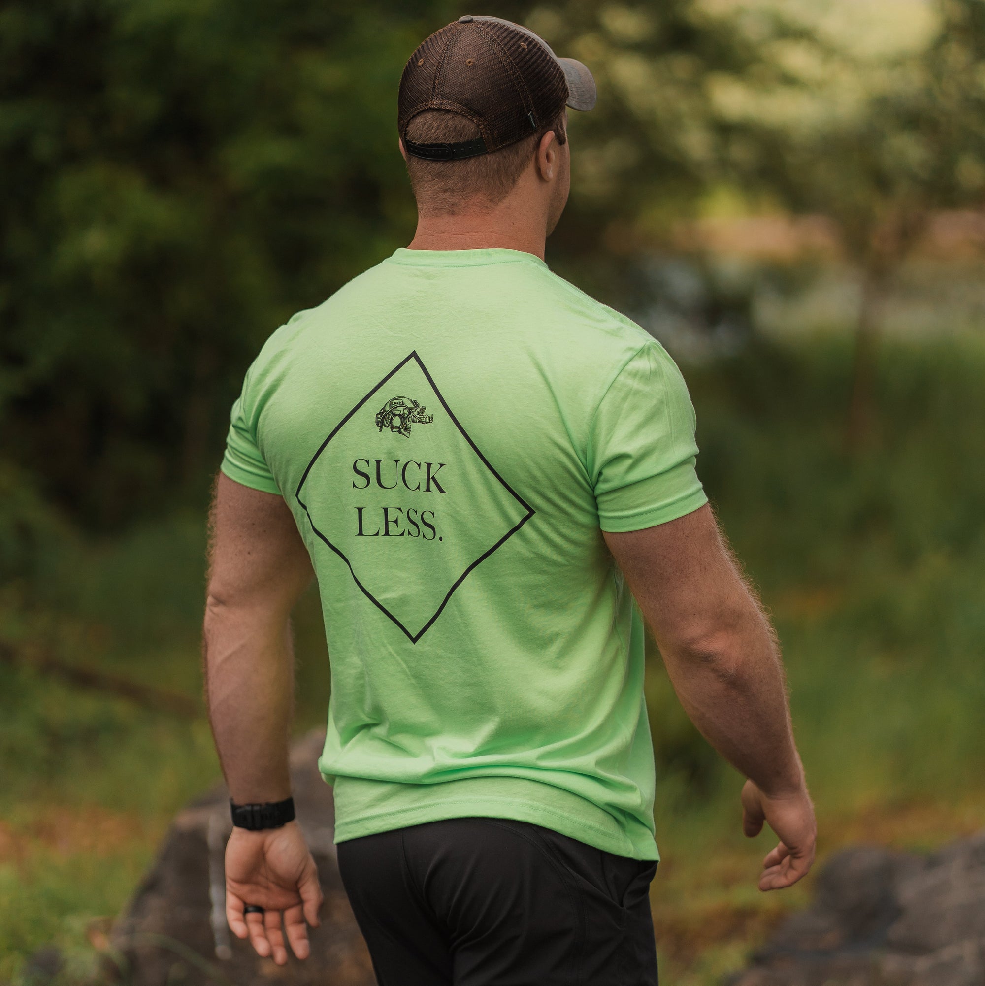 Man wearing a neon green t-shirt with 'Suck Less' text walking outdoors.