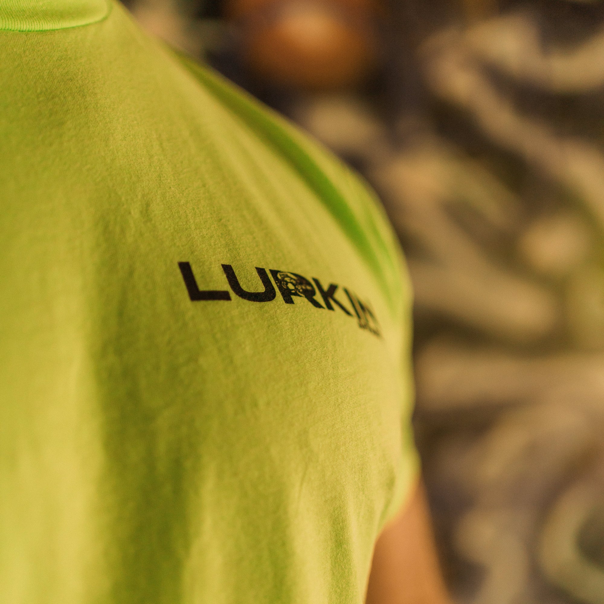 Person wearing a neon green t-shirt with 'Lurkin' logo, blurred background